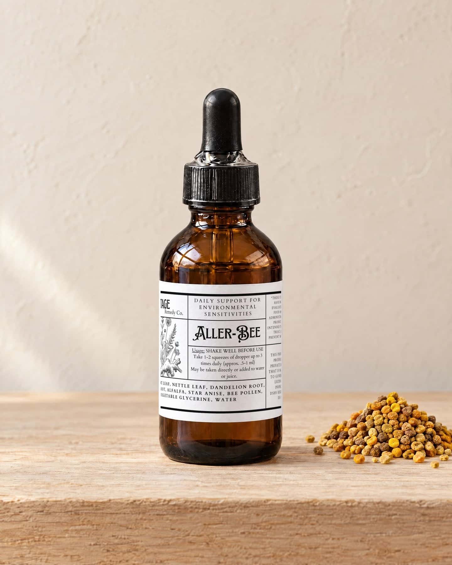 A dropper bottle of Aller-Bee Botanical Drops on a pale oak shelf, a small heap of golden bee pollen granules beside it