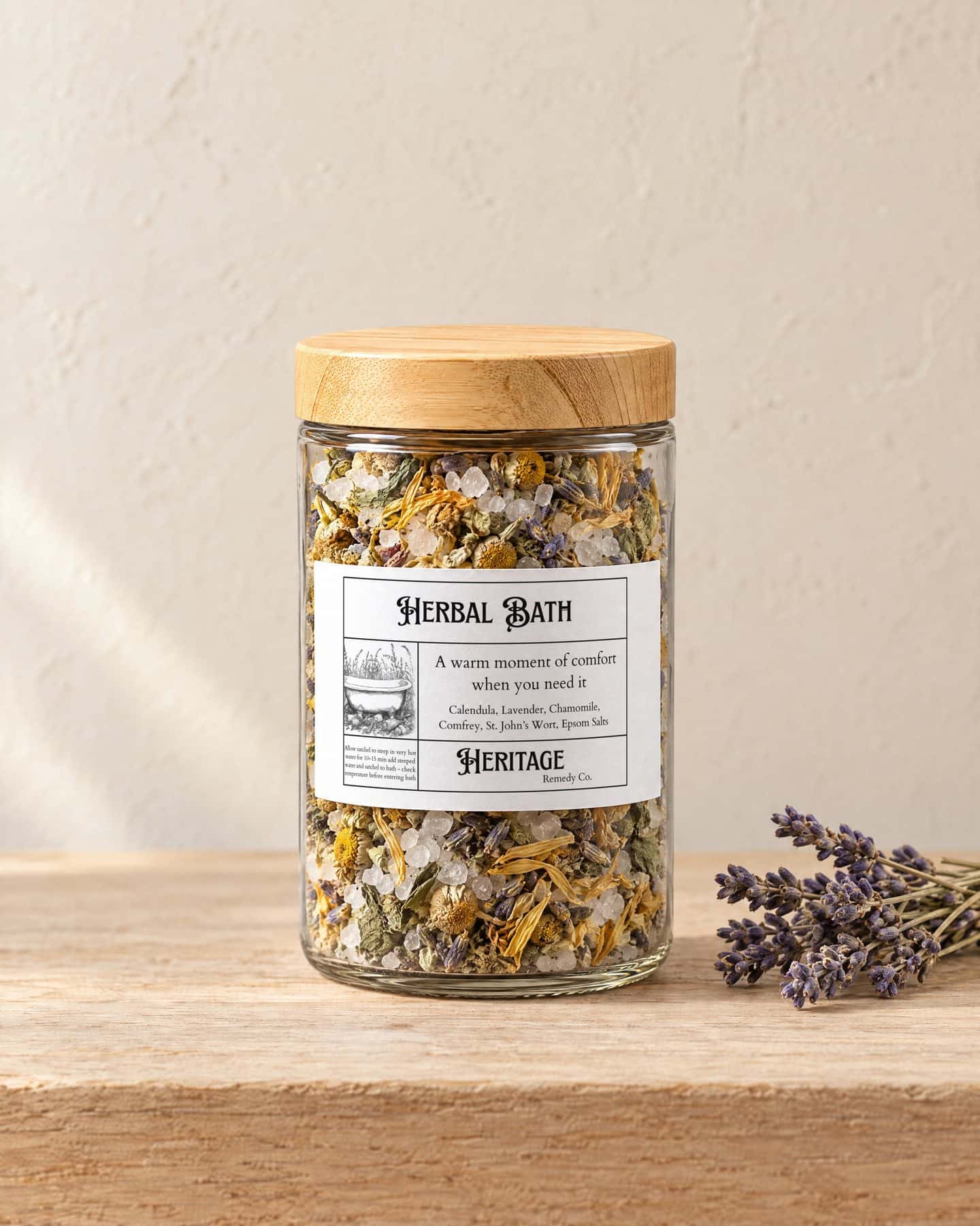A jar of Herbal Bath Blend with a bamboo lid on a pale oak shelf, a small bundle of dried lavender beside it