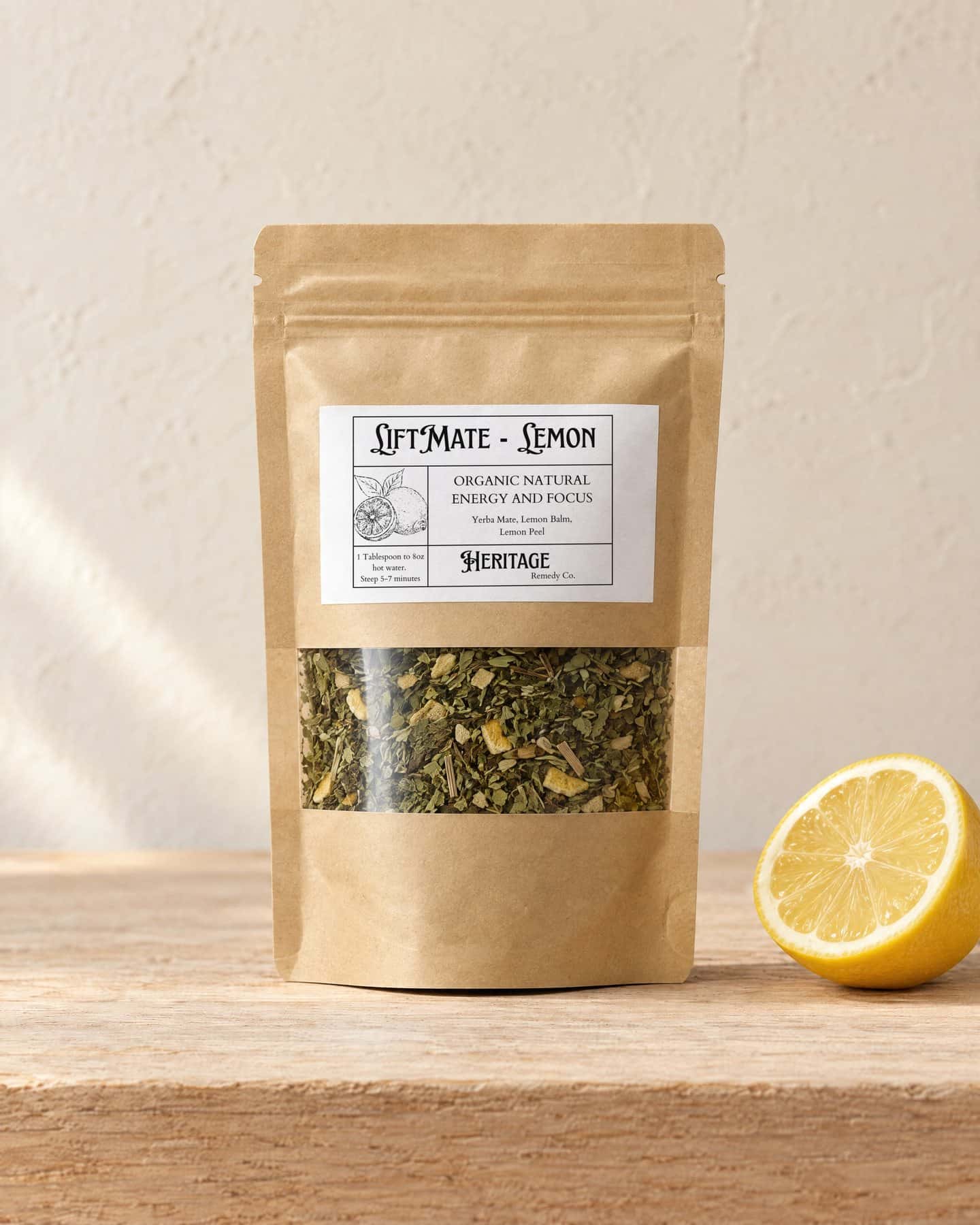 A kraft pouch of LiftMate - Lemon with a window onto the loose tea, on a pale oak shelf, a fresh lemon cut in half beside it