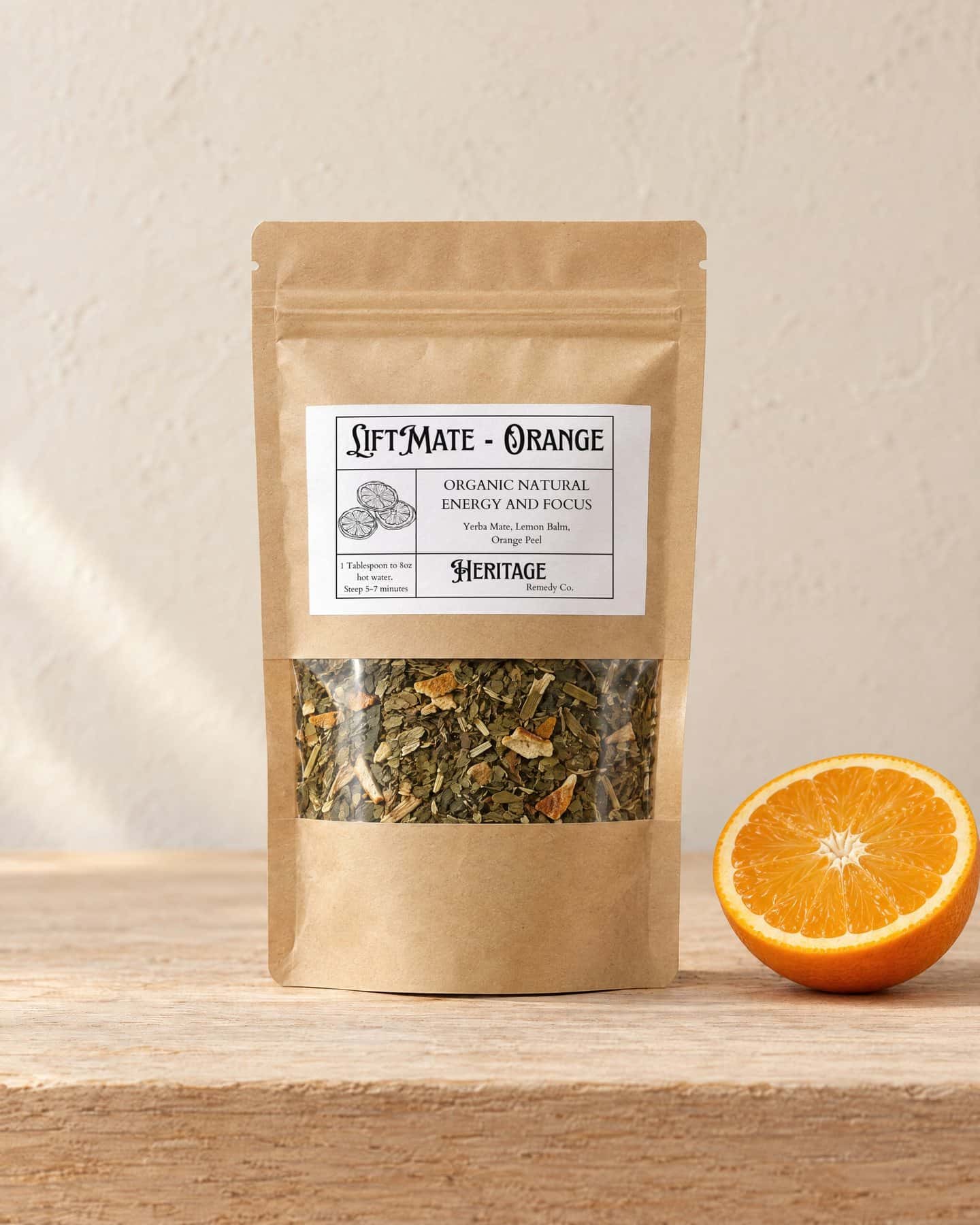 A kraft pouch of LiftMate - Orange with a window onto the loose tea, on a pale oak shelf, a fresh orange cut in half beside it