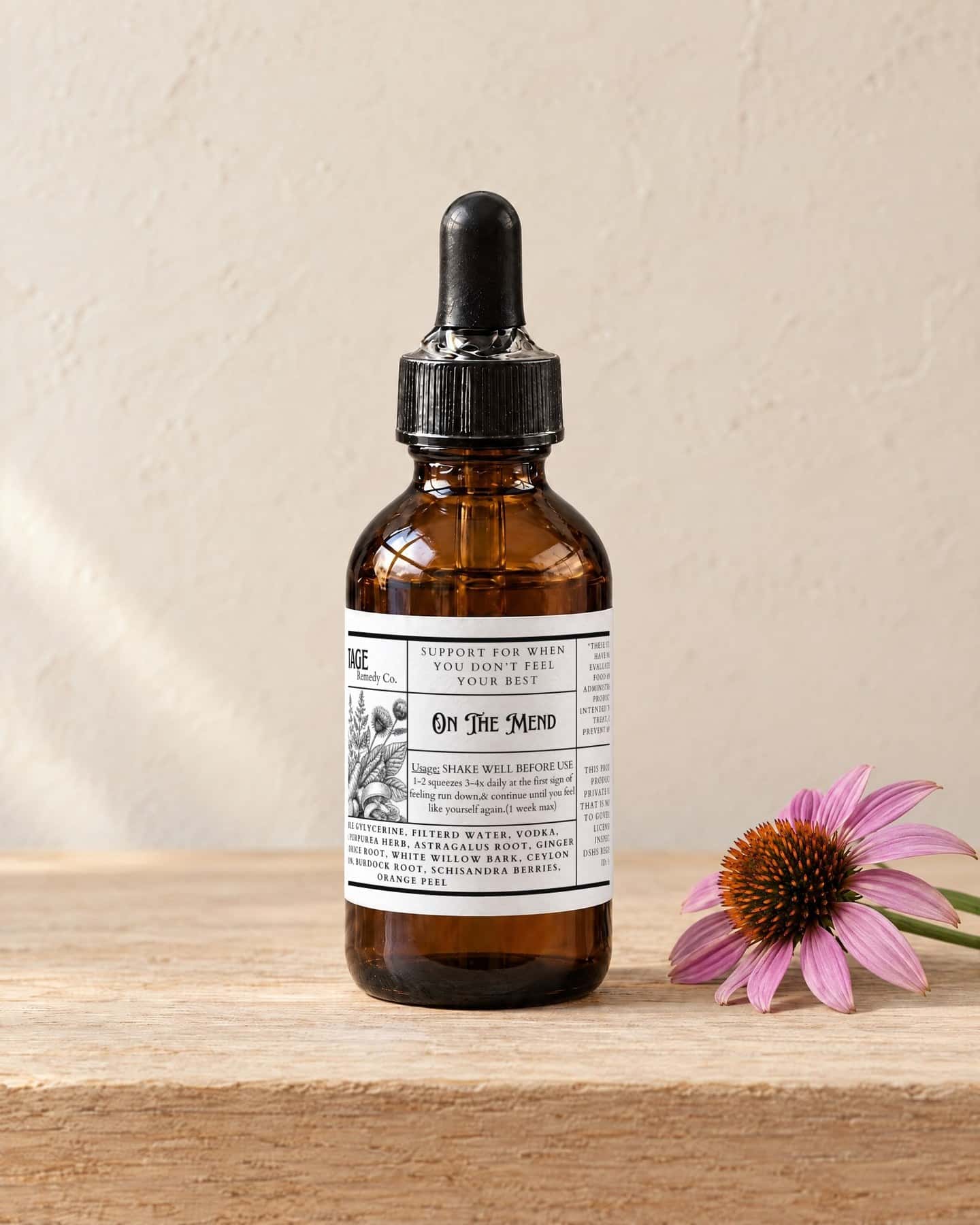 A dropper bottle of On The Mend - Adults on a pale oak shelf, a purple coneflower bloom beside it
