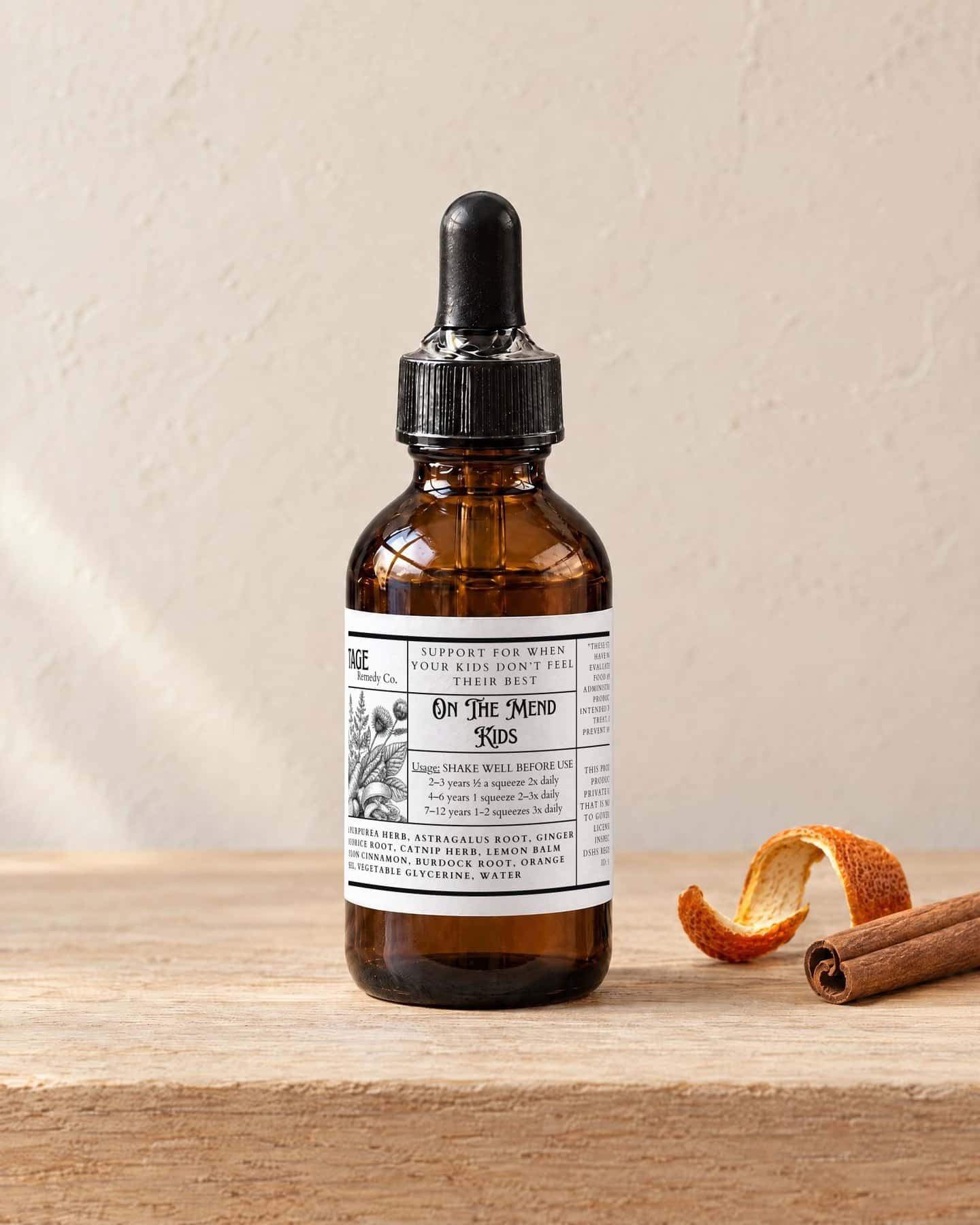 A dropper bottle of On The Mend - Kids on a pale oak shelf, a curl of dried orange peel and a Ceylon cinnamon stick beside it