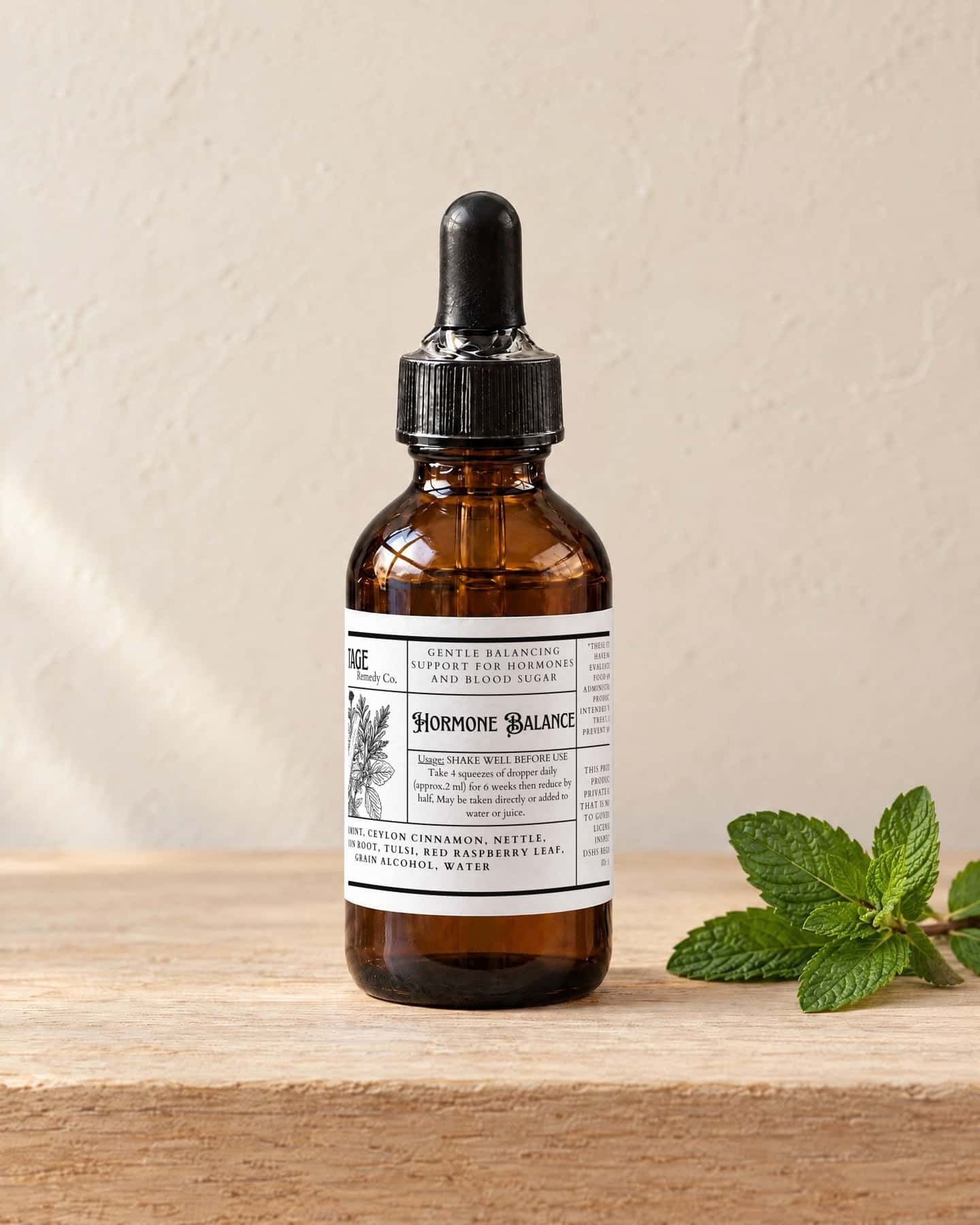 A dropper bottle of Hormone Balance on a pale oak shelf, a sprig of fresh spearmint beside it