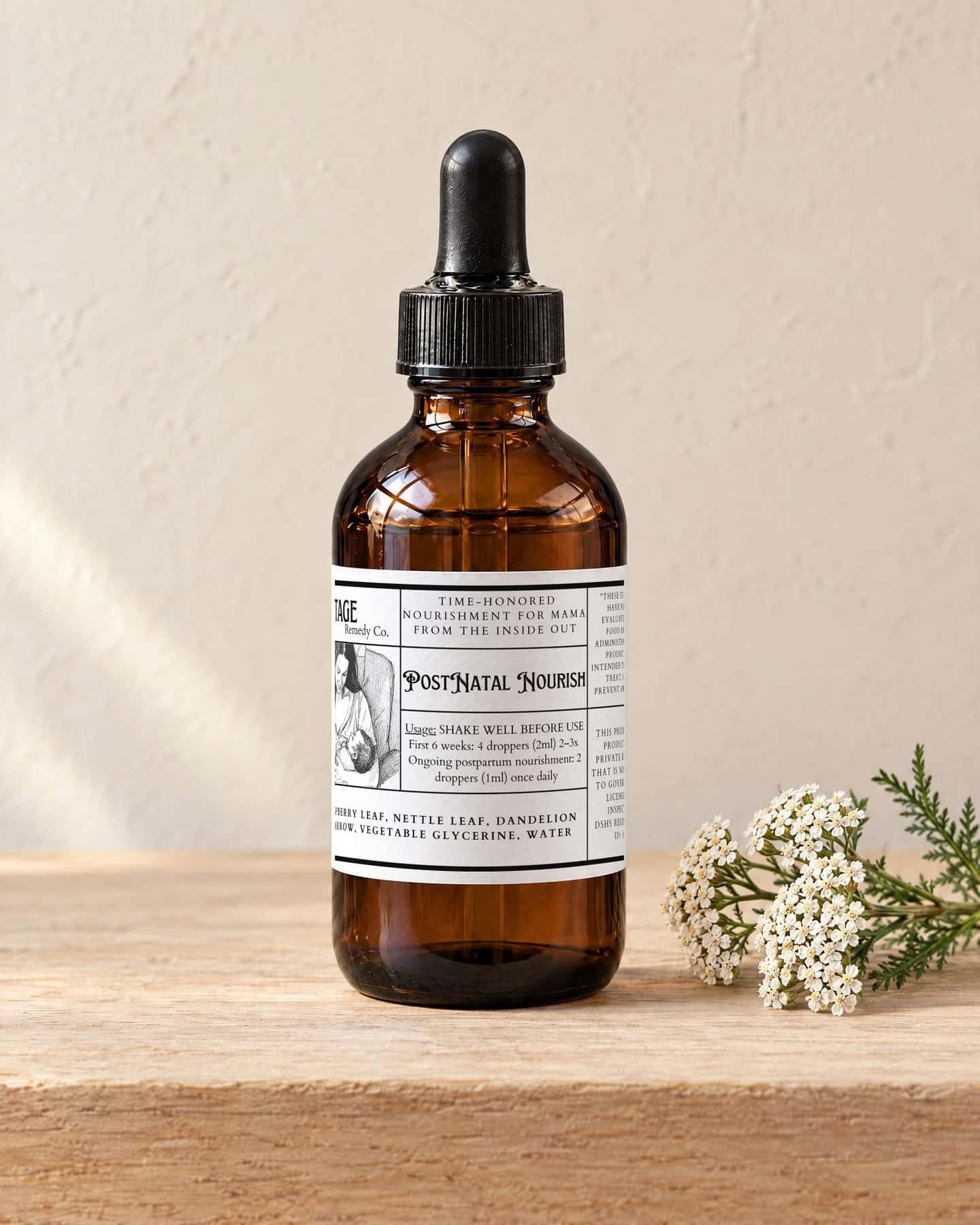 A four ounce dropper bottle of PostNatal Nourish on a pale oak shelf, a sprig of white yarrow flowers beside it