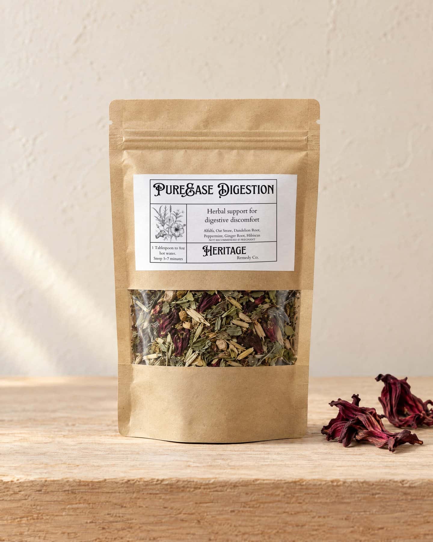 A kraft pouch of PureEase Digestion with a window onto the loose tea, on a pale oak shelf, a few dried deep red hibiscus flowers beside it