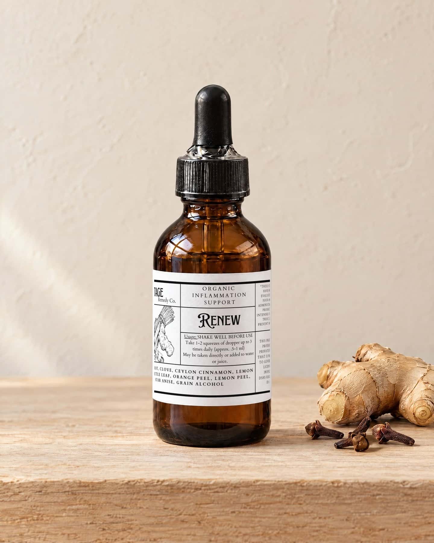A dropper bottle of Renew Tincture on a pale oak shelf, a knob of fresh ginger root and a few whole cloves beside it
