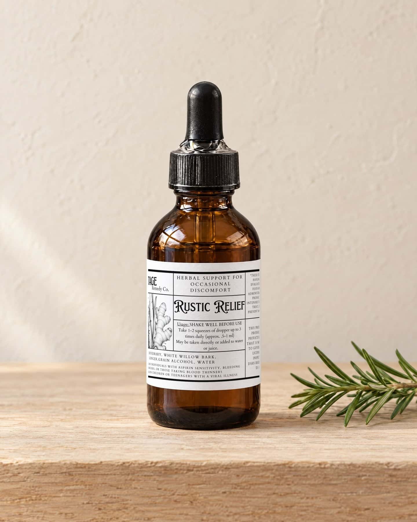 A dropper bottle of Rustic Relief Tincture on a pale oak shelf, a sprig of fresh rosemary beside it