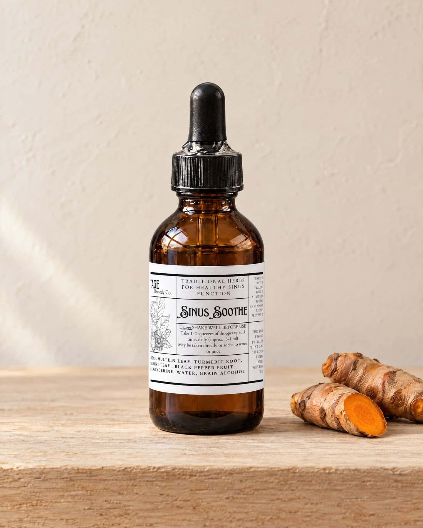 A dropper bottle of Sinus Soothe on a pale oak shelf, two pieces of fresh turmeric root beside it